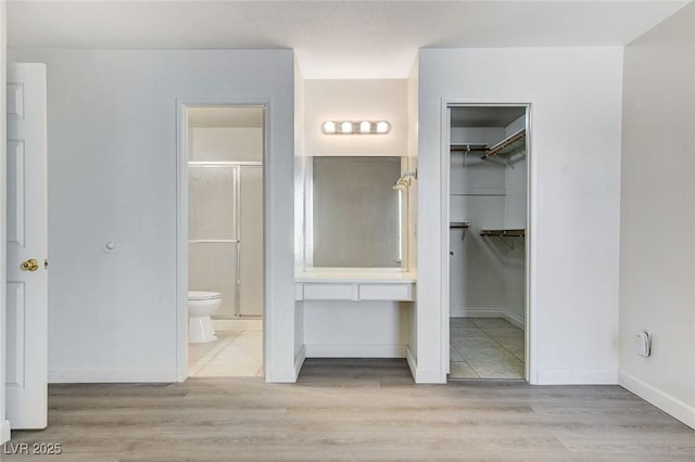 unfurnished bedroom featuring a spacious closet, wood finished floors, baseboards, and ensuite bathroom