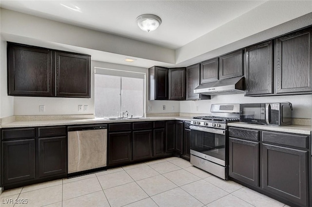 kitchen featuring under cabinet range hood, a sink, appliances with stainless steel finishes, light tile patterned flooring, and light countertops