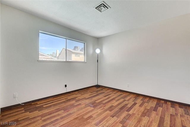 empty room with visible vents, baseboards, a textured ceiling, and wood finished floors