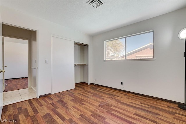 unfurnished bedroom featuring wood finished floors, visible vents, a closet, and a textured ceiling