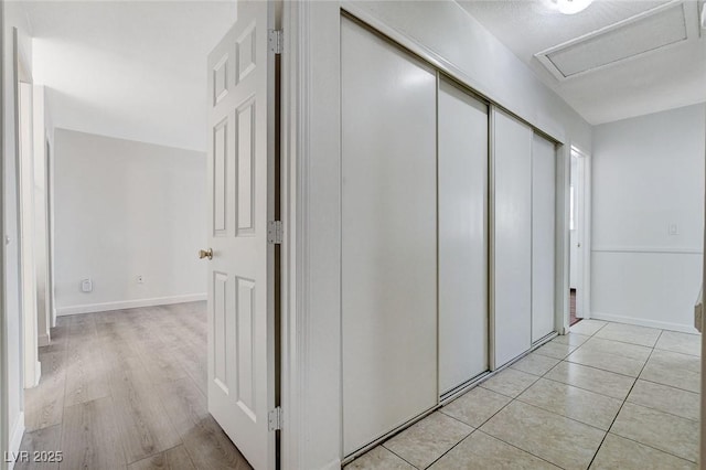 corridor featuring light tile patterned floors, attic access, and baseboards