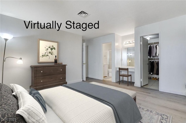 bedroom featuring wood finished floors, visible vents, baseboards, ensuite bath, and a walk in closet