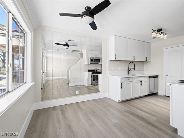 kitchen with light countertops, light wood-style flooring, appliances with stainless steel finishes, a ceiling fan, and a sink