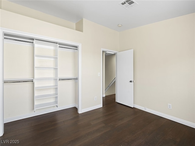 unfurnished bedroom with dark wood-style floors, visible vents, baseboards, and a closet