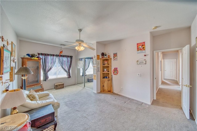 living area with baseboards, light carpet, a textured ceiling, and ceiling fan