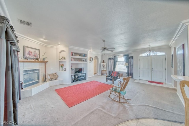 carpeted living area with visible vents, built in shelves, arched walkways, crown molding, and a tile fireplace