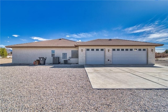 ranch-style home featuring a tiled roof, concrete driveway, central AC unit, stucco siding, and a garage