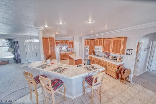 kitchen with white appliances, a peninsula, arched walkways, ornamental molding, and light colored carpet