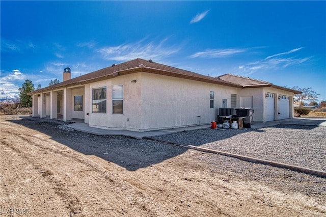 view of side of property with a garage, concrete driveway, a chimney, and stucco siding