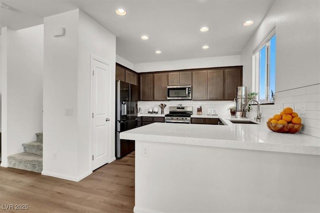 kitchen featuring light wood-style flooring, a sink, stainless steel appliances, dark brown cabinetry, and light countertops