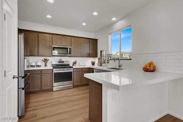 kitchen featuring a sink, a peninsula, light wood-style floors, and stainless steel appliances