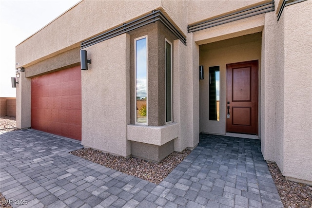 doorway to property featuring stucco siding, driveway, and a garage