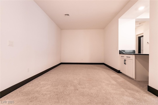 empty room featuring light carpet, visible vents, and baseboards