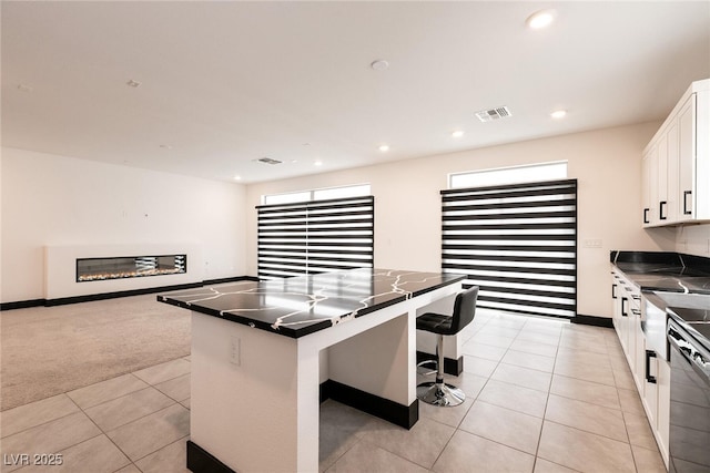 kitchen featuring visible vents, dark countertops, white cabinets, light tile patterned floors, and dishwasher