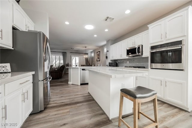 kitchen featuring visible vents, light wood-type flooring, appliances with stainless steel finishes, a peninsula, and white cabinets