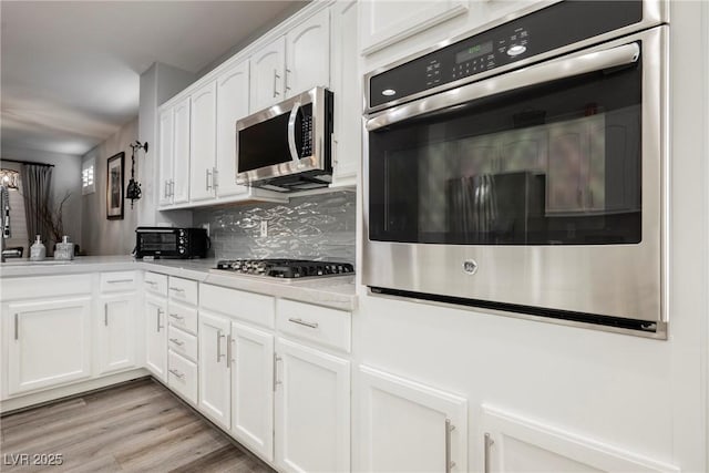 kitchen featuring decorative backsplash, light countertops, white cabinets, appliances with stainless steel finishes, and light wood-type flooring