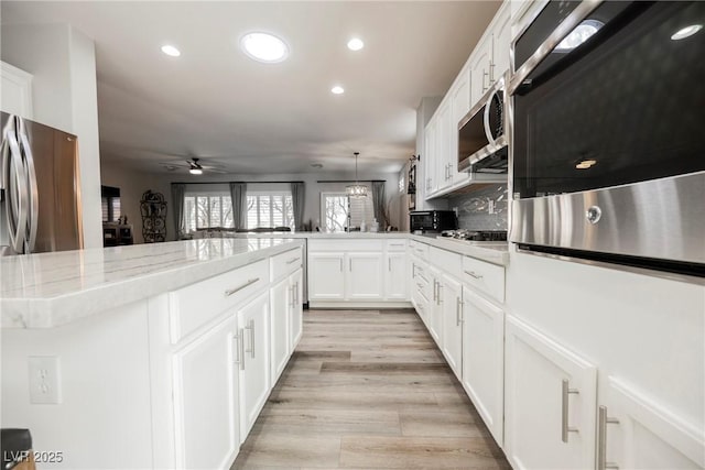 kitchen with a ceiling fan, a peninsula, light wood-style flooring, stainless steel appliances, and white cabinetry