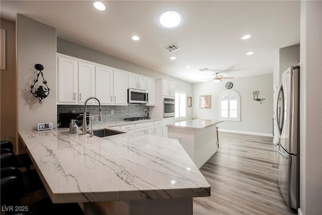 kitchen featuring visible vents, a kitchen island, a peninsula, a sink, and appliances with stainless steel finishes