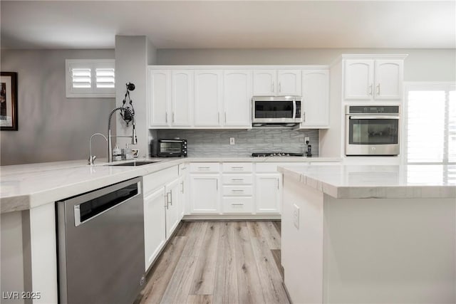 kitchen featuring light stone countertops, a sink, stainless steel appliances, white cabinetry, and light wood-type flooring