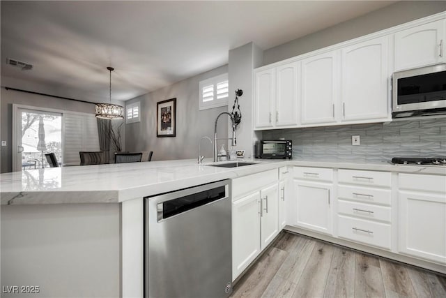 kitchen featuring light stone counters, visible vents, a peninsula, a sink, and stainless steel appliances