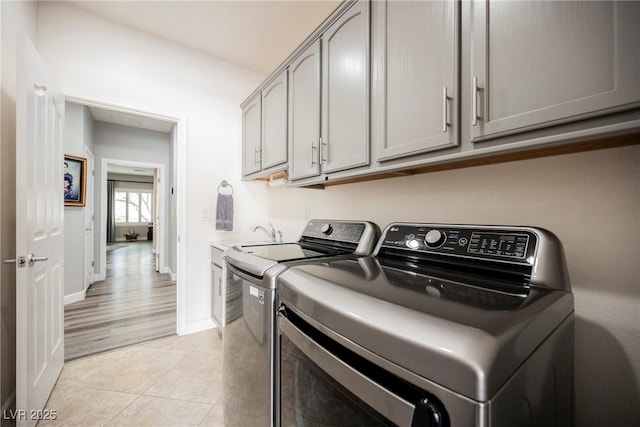 washroom featuring light tile patterned floors, baseboards, cabinet space, and washing machine and dryer