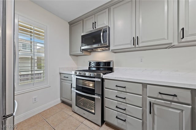 kitchen featuring light tile patterned floors, gray cabinets, appliances with stainless steel finishes, and baseboards