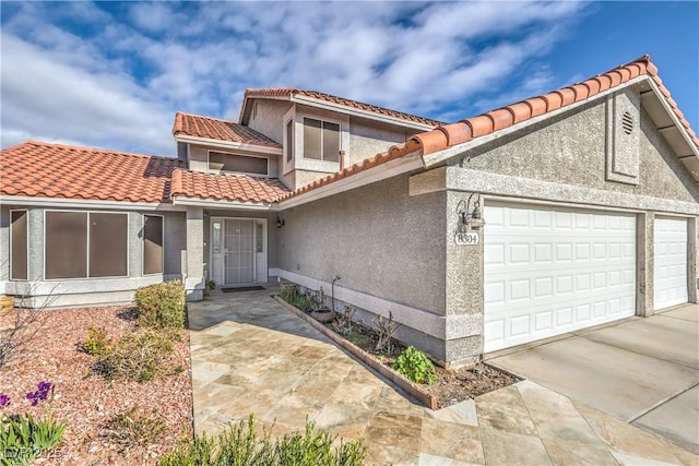 view of front facade featuring a tiled roof, an attached garage, driveway, and stucco siding