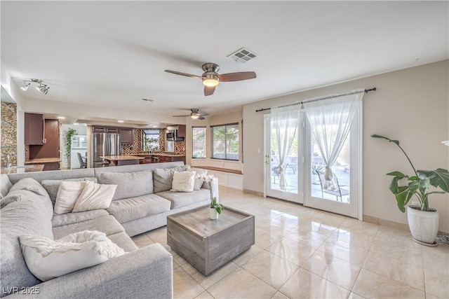 living area featuring light tile patterned floors, visible vents, baseboards, and a ceiling fan