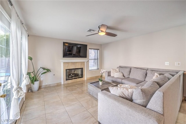 living area with visible vents, baseboards, a tiled fireplace, light tile patterned floors, and a ceiling fan