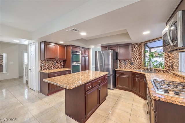 kitchen featuring visible vents, a kitchen island, appliances with stainless steel finishes, a raised ceiling, and a sink