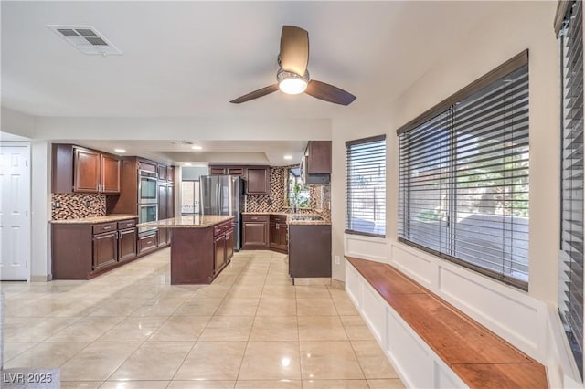 kitchen with tasteful backsplash, visible vents, a kitchen island, ceiling fan, and appliances with stainless steel finishes