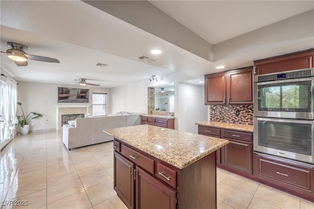 kitchen featuring visible vents, a kitchen island, stainless steel double oven, ceiling fan, and backsplash