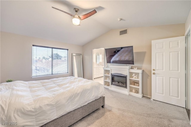 carpeted bedroom featuring visible vents, ceiling fan, vaulted ceiling, ensuite bathroom, and a glass covered fireplace