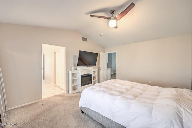 bedroom with visible vents, vaulted ceiling, light carpet, a glass covered fireplace, and a ceiling fan