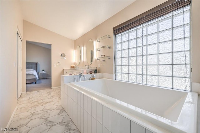 bathroom featuring vanity, vaulted ceiling, tiled tub, and connected bathroom