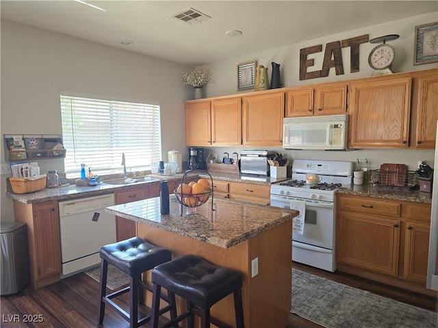 kitchen featuring visible vents, a center island, a kitchen bar, white appliances, and a sink