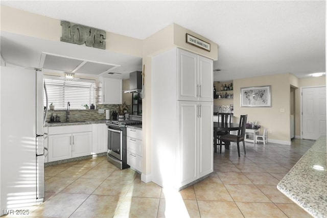3258 Del Marino St, Las Vegas, NV 89121 - kitchen featuring stainless steel range with gas stovetop, freestanding refrigerator, light tile patterned floors, wall chimney range hood, and white cabinets