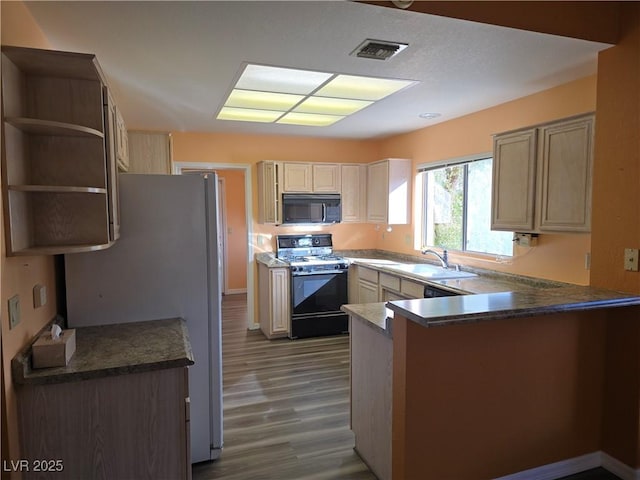 kitchen with range with gas stovetop, a peninsula, freestanding refrigerator, a sink, and black microwave