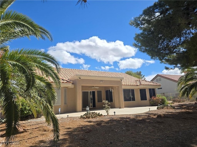 rear view of house with a tiled roof, a patio, stucco siding, and fence