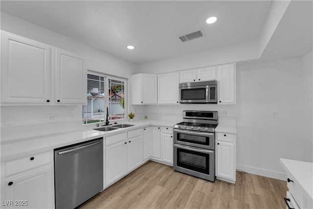 kitchen featuring light wood finished floors, visible vents, appliances with stainless steel finishes, white cabinetry, and a sink