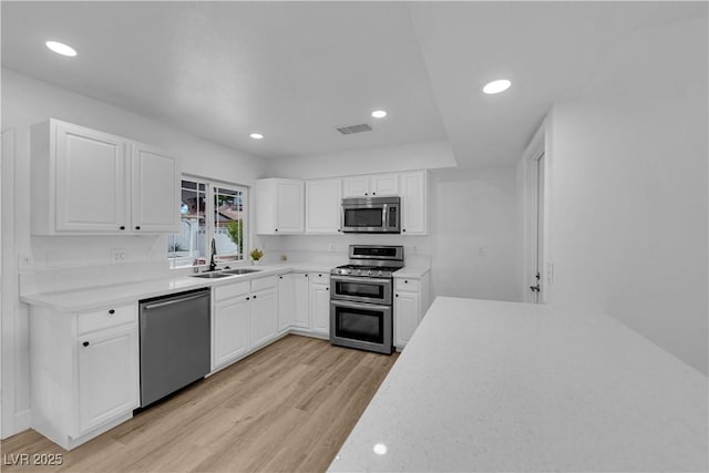 kitchen featuring a sink, light countertops, appliances with stainless steel finishes, white cabinetry, and light wood-type flooring