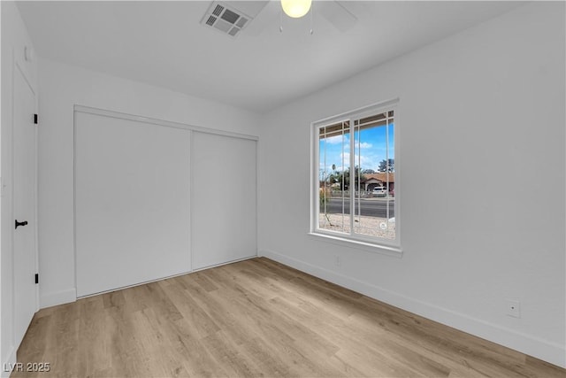 unfurnished bedroom featuring a ceiling fan, baseboards, visible vents, light wood-style flooring, and a closet