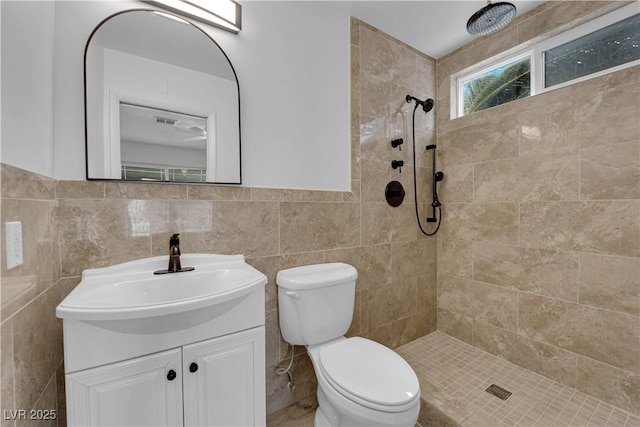 full bathroom with vanity, tiled shower, wainscoting, tile walls, and toilet