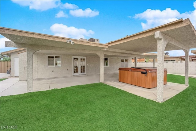 rear view of house featuring fence, stucco siding, a hot tub, a patio area, and a lawn