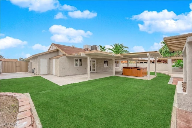 rear view of property with a yard, a patio, fence, and a hot tub