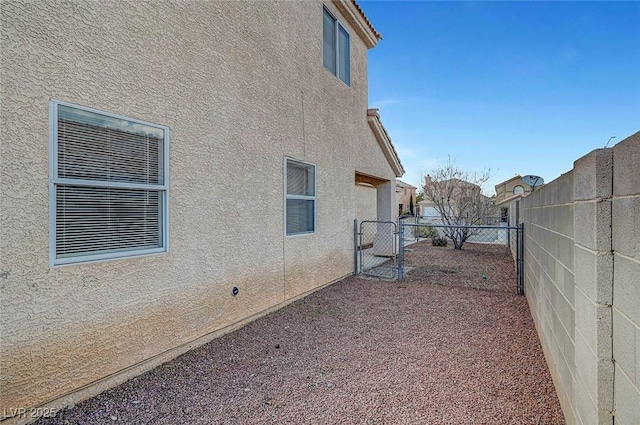 view of property exterior featuring stucco siding, a fenced backyard, and a gate