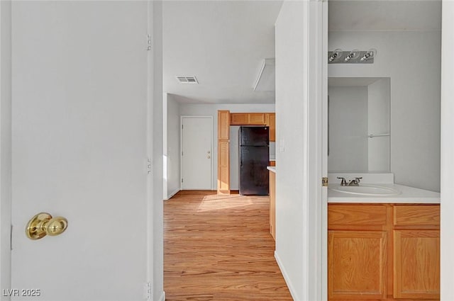 hallway with visible vents, light wood-style floors, and a sink