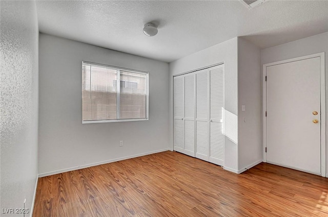 unfurnished bedroom featuring a closet, baseboards, a textured ceiling, and wood finished floors