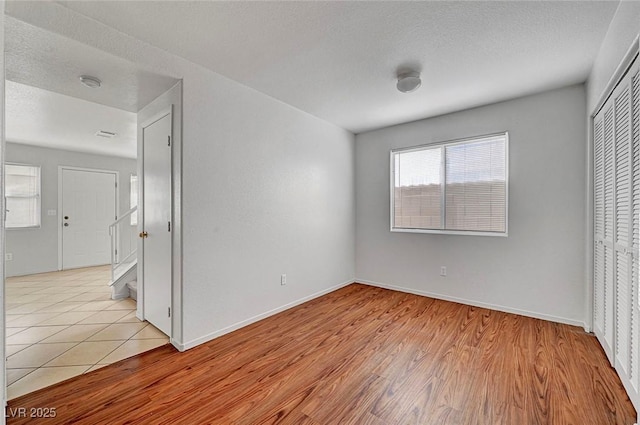 unfurnished bedroom featuring baseboards, a closet, light wood finished floors, and a textured ceiling