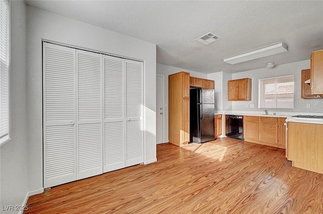 kitchen featuring visible vents, a sink, black appliances, light countertops, and light wood-style floors